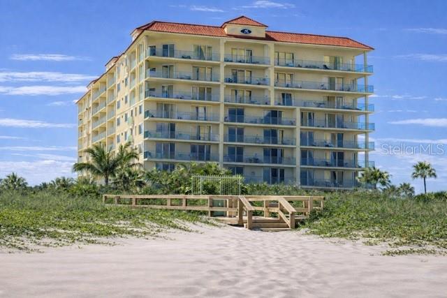 A multi-story beachfront condominium building stands behind a wooden boardwalk and sandy dunes — 420 HARDING AVENUE UNIT 301, COCOA BEACH, FL