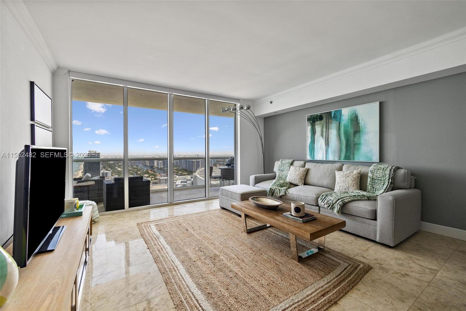 A living room features a grey sofa, wooden coffee table, and floor-to-ceiling windows with views — 1830 S Ocean Dr # 5005, Hallandale Beach FL 33009, HALLANDALE BEACH, FL