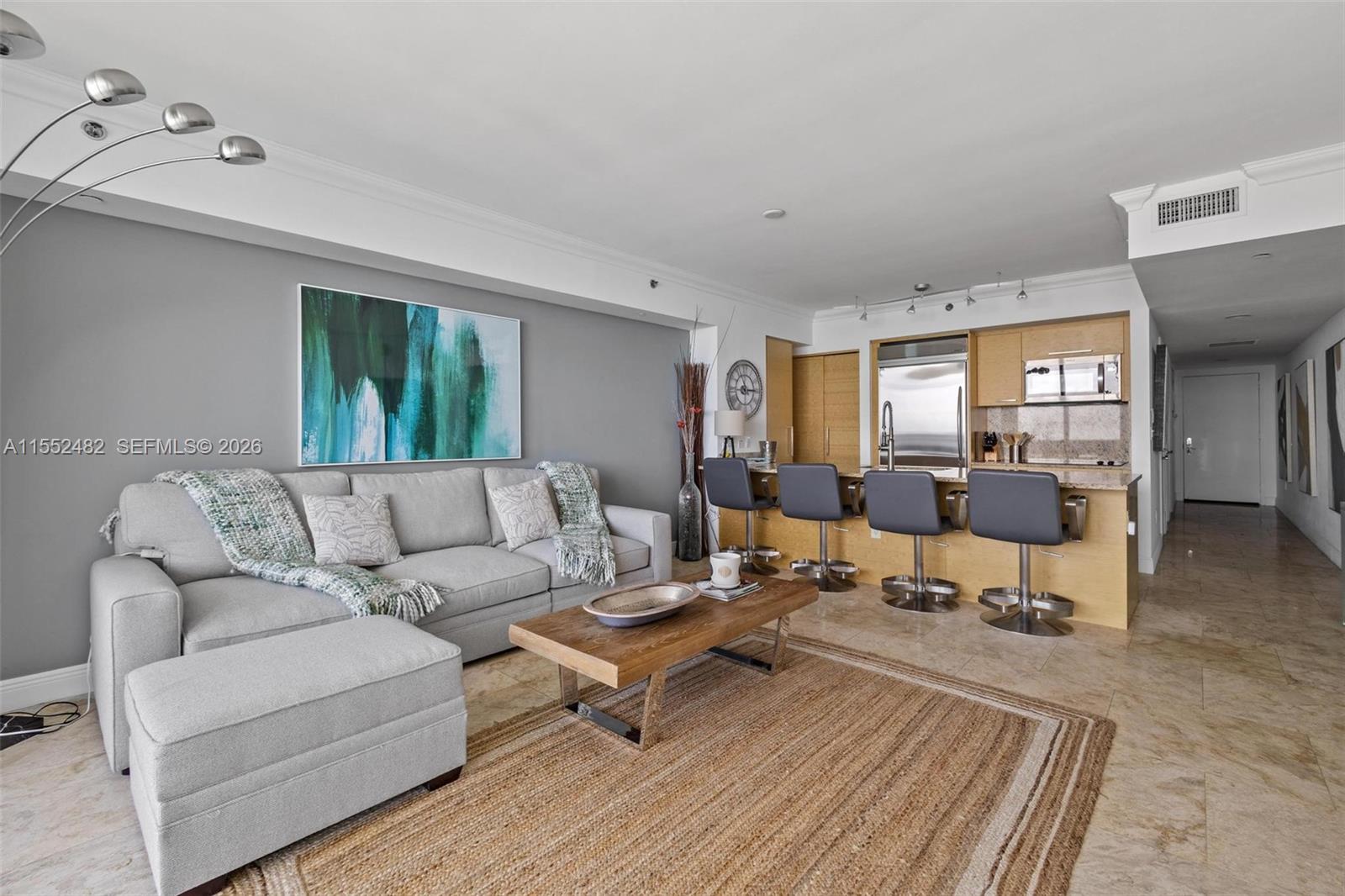 A living room and kitchen area with a gray sofa, wooden coffee table, and bar stools — 1830 S Ocean Dr # 5005, Hallandale Beach FL 33009, HALLANDALE BEACH, FL
