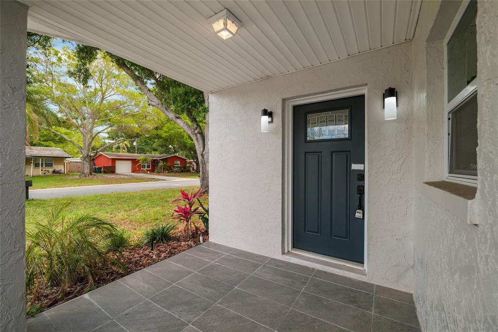 A covered front porch with gray tile flooring leads to a dark blue front door — 2952 WEBLEY DRIVE, LARGO, FL
