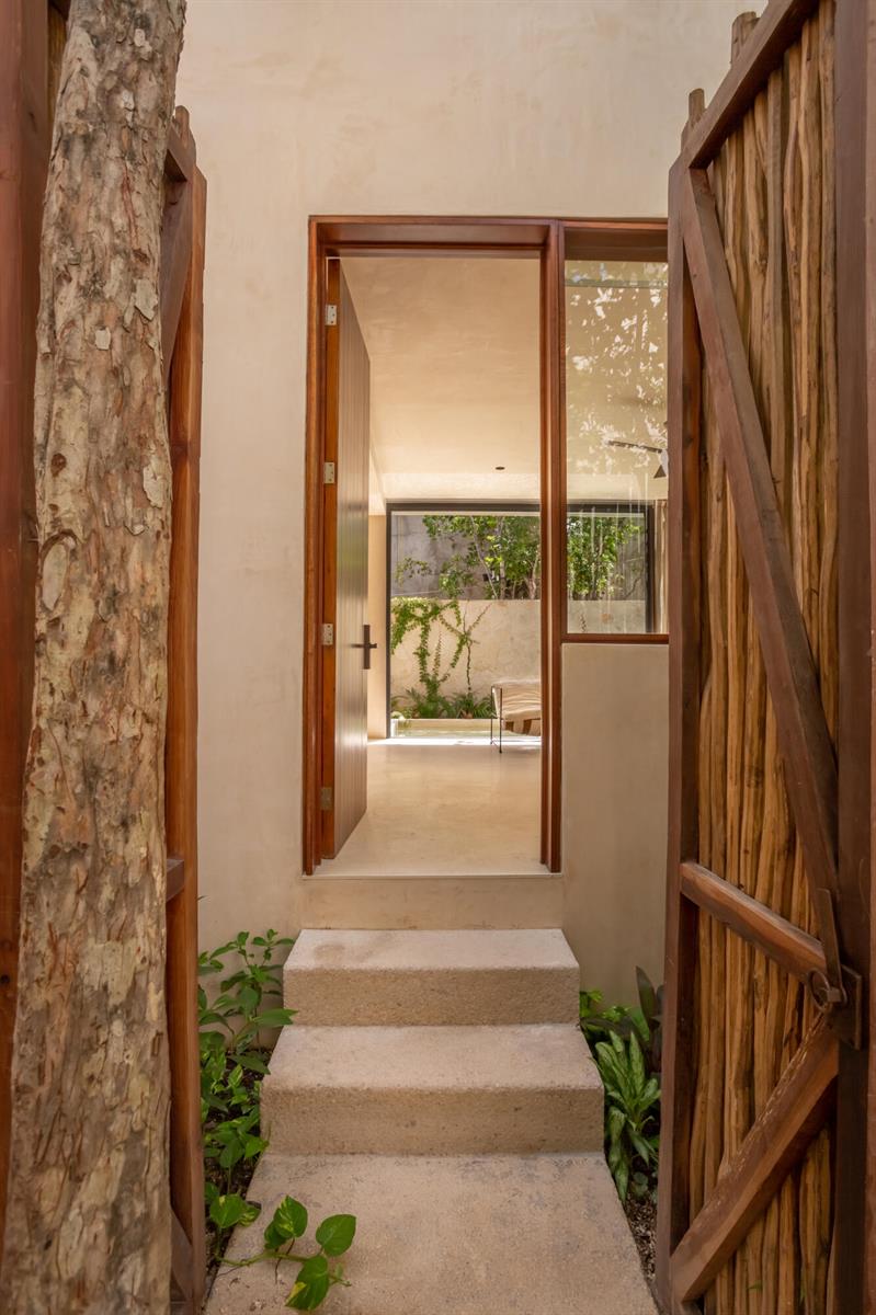 A stone staircase leads through a wooden gate into a bright room with glass walls — Amari Tulum 10 Avenida Norte & Calle Palma, FL