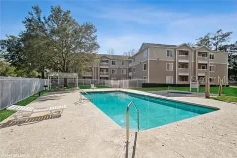 An outdoor swimming pool sits in front of a multi-story apartment building under a blue sky — 4000 SW 23RD STREET UNIT 4-103, #4, GAINESVILLE, FL