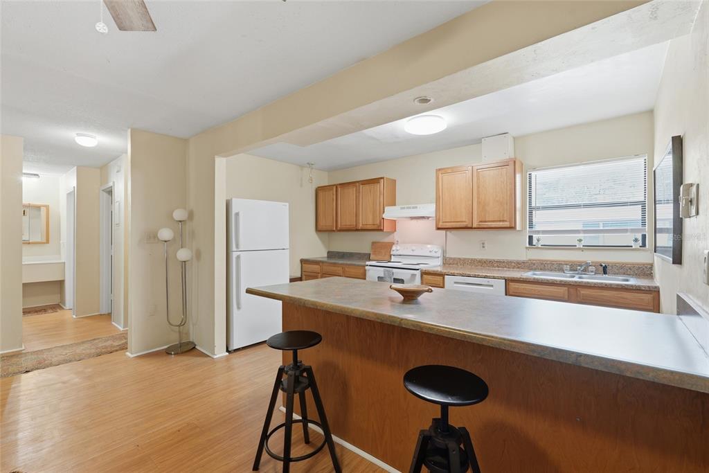 A kitchen features wooden cabinets, a breakfast bar with two stools, and light-colored flooring — 2811 SW ARCHER ROAD UNIT Y232, GAINESVILLE, FL