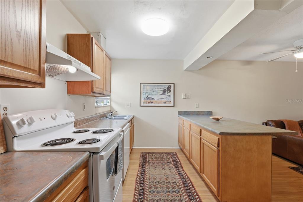 A kitchen features wood cabinets, laminate countertops, a white electric range, and a runner rug — 2811 SW ARCHER ROAD UNIT Y232, GAINESVILLE, FL