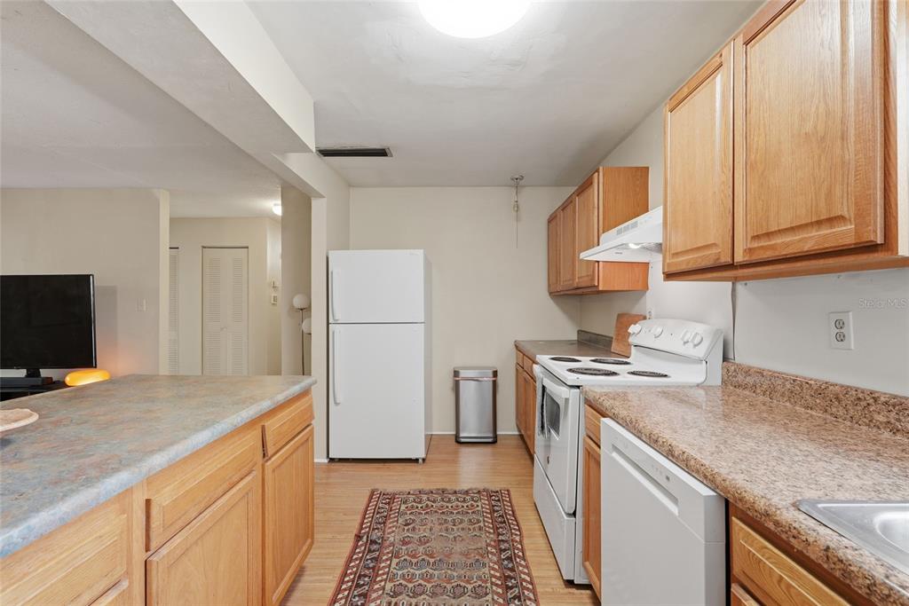 A kitchen features wood cabinets, laminate countertops, white appliances, and a patterned area rug — 2811 SW ARCHER ROAD UNIT Y232, GAINESVILLE, FL