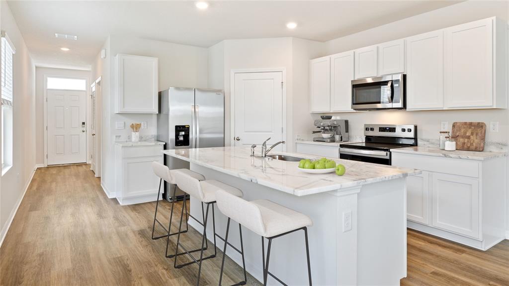 A modern kitchen features white cabinets, a marble-topped island with bar stools, and stainless appliances — 2459 25TH AVENUE S, ST PETERSBURG, FL