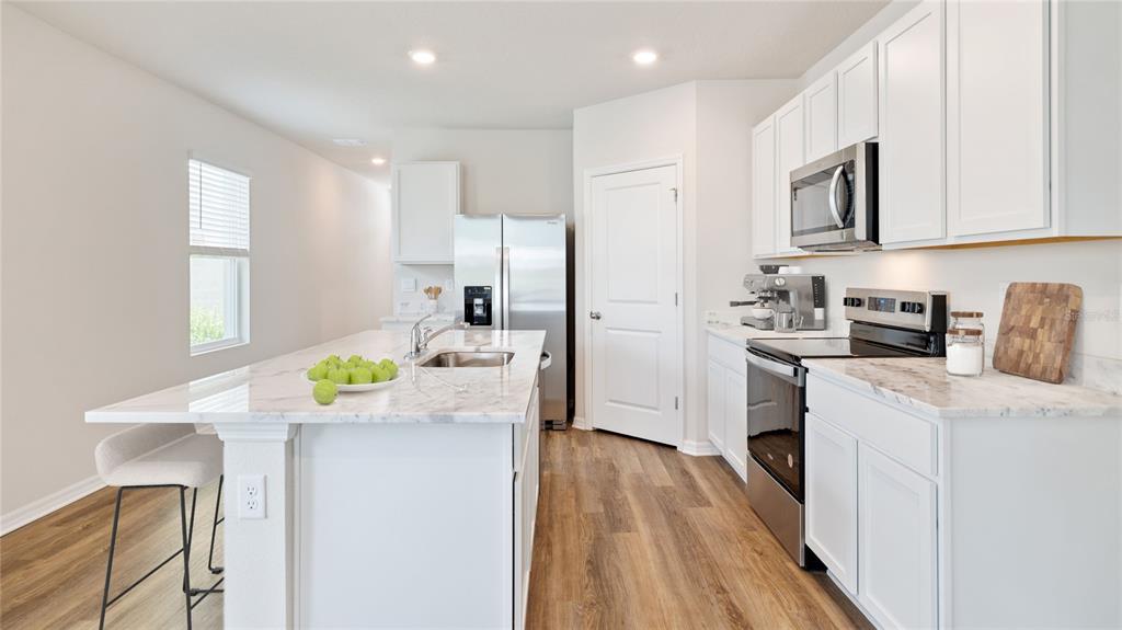 A kitchen features white cabinets, marble-look countertops, stainless steel appliances, and wood-style flooring — 2459 25TH AVENUE S, ST PETERSBURG, FL