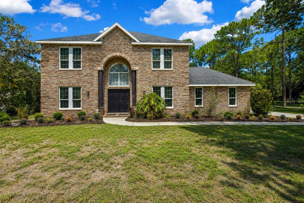 A two-story brick house with a central arched entryway and a large front lawn — 7377 ROYAL OAK DRIVE, WEEKI WACHEE, FL