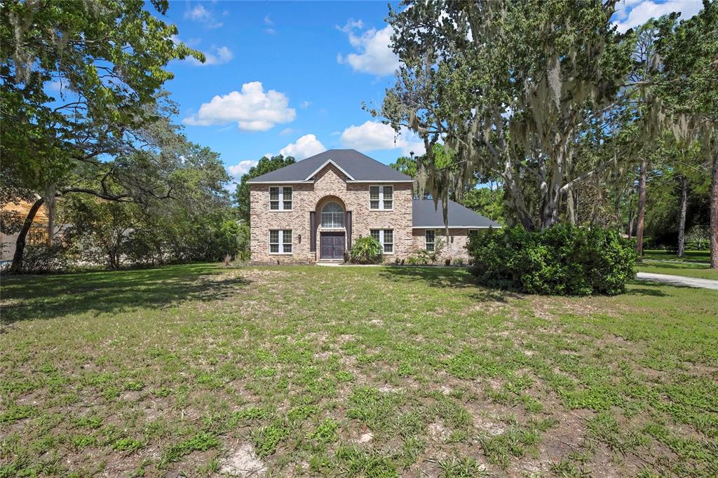 A two-story brick house with a dark roof sits on a large, grassy lot — 7377 ROYAL OAK DRIVE, WEEKI WACHEE, FL