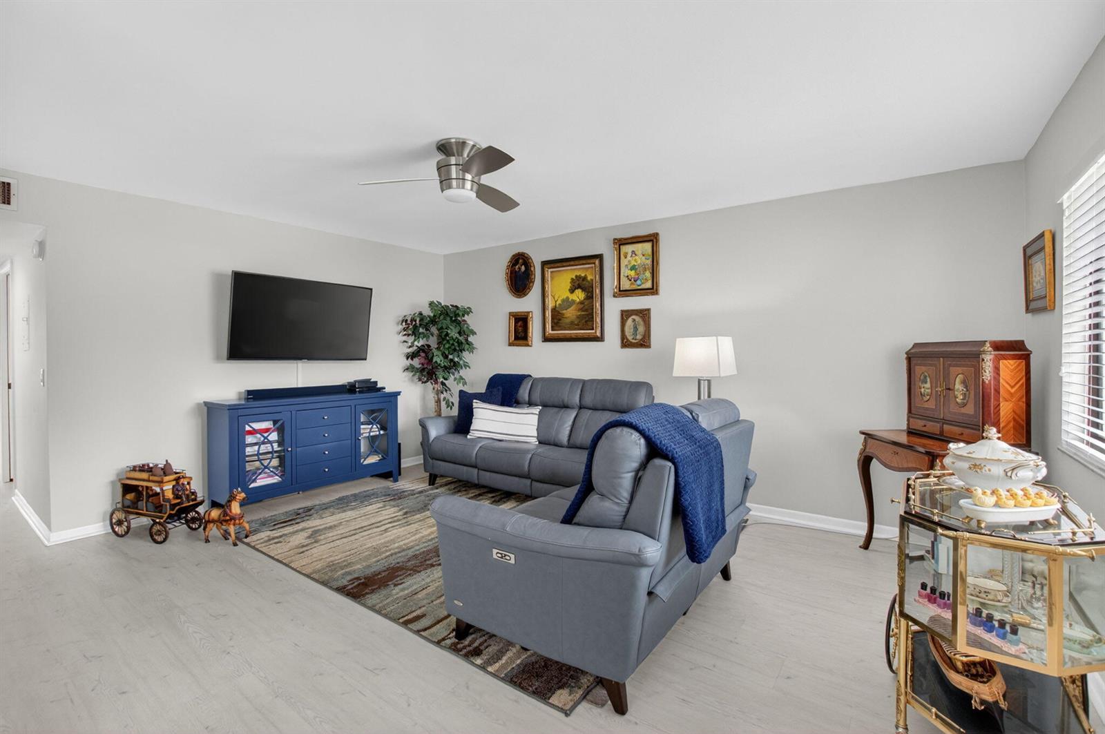 A living room features gray leather sofas, a blue media console, and a patterned rug — 15054 Ashland Way # 82, Delray Beach FL 33484, DELRAY BEACH, FL