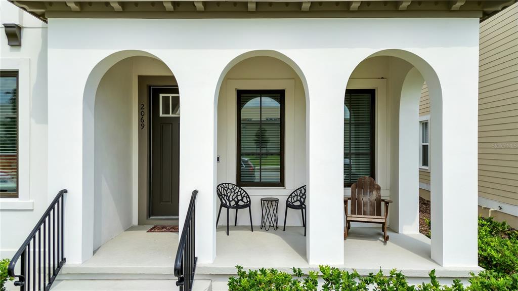 A covered front porch features three white arches, a dark door, and outdoor seating — 2069 CELEBRATION BOULEVARD, KISSIMMEE, FL