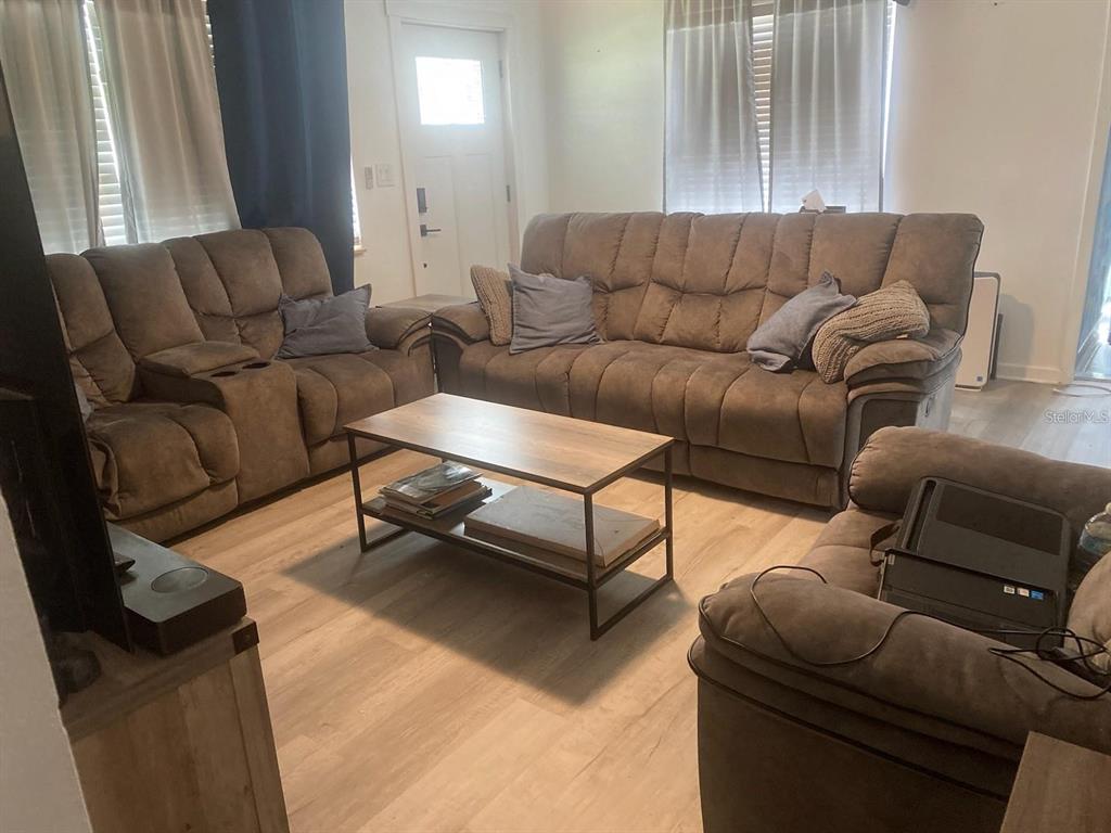 A living room features brown reclining sofas, a metal-framed coffee table, and light wood flooring — 1110 E EDGEWOOD DRIVE, LAKELAND, FL