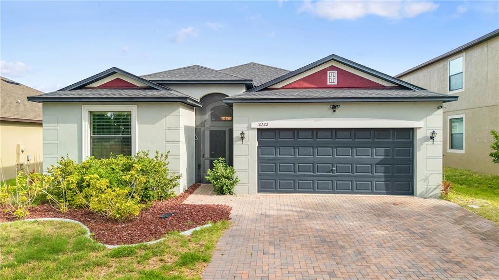 A single-story house with a gray garage, red gable accents, and a brick paver driveway — 10222 CELTIC ASH DRIVE, RUSKIN, FL