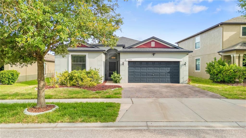 A single-story house with a dark garage door, a front porch, and a paved driveway — 10222 CELTIC ASH DRIVE, RUSKIN, FL
