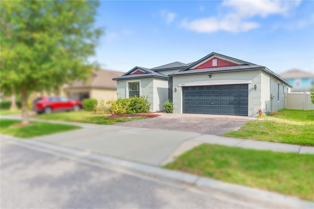 A single-story house with a dark garage door, light-colored stucco walls, and a red gable — 10222 CELTIC ASH DRIVE, RUSKIN, FL