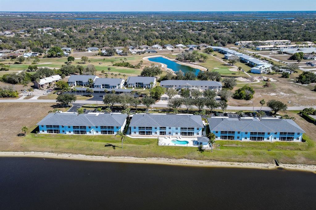 An aerial view shows multi-story apartment buildings with a swimming pool situated along a lake — 1479 SAN CRISTOBAL AVENUE UNIT 2104, PUNTA GORDA, FL