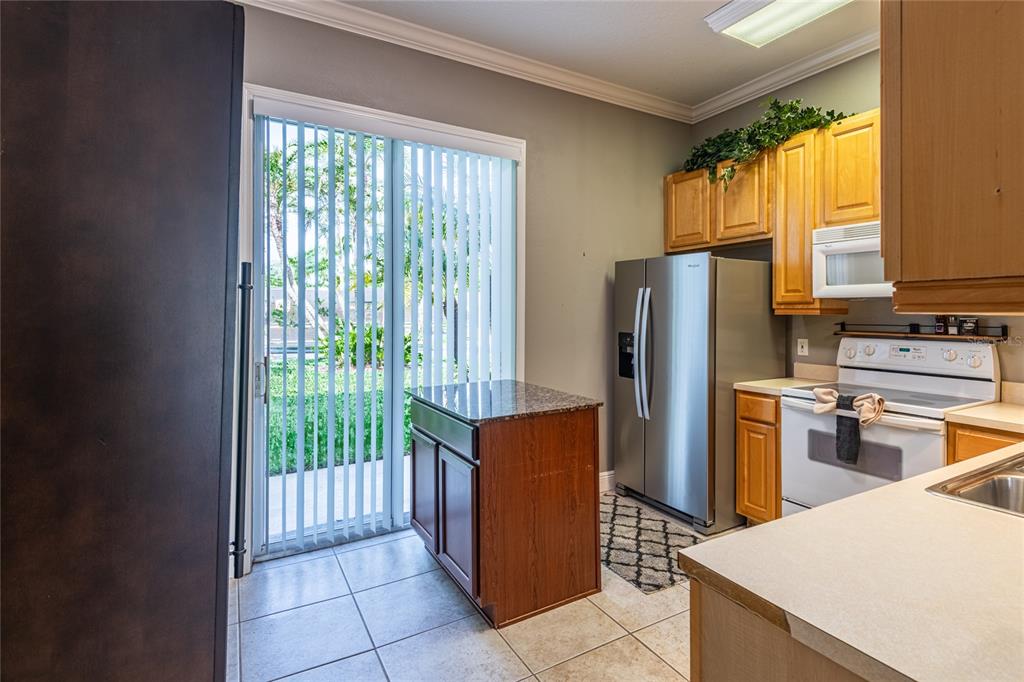 A kitchen features wood cabinets, stainless steel appliances, a small island, and a sliding glass door — 6714 DALI AVENUE UNIT 101, LAND O LAKES, FL