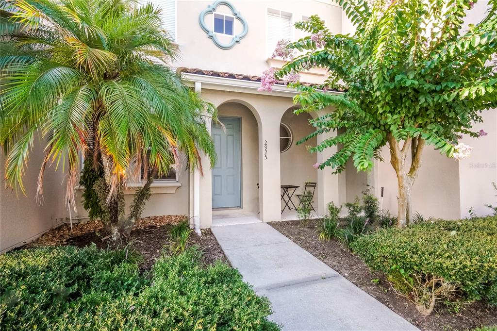 A beige two-story townhouse exterior features a blue front door, arched entryway, and palm tree — 2925 AQUA VIRGO LOOP UNIT 25, ORLANDO, FL