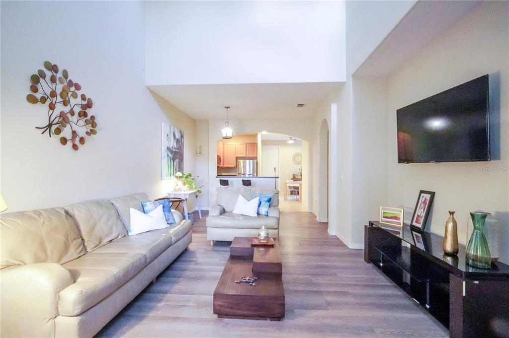 A living room features light wood-look flooring, a beige sofa, and a wall-mounted television — 2925 AQUA VIRGO LOOP UNIT 25, ORLANDO, FL