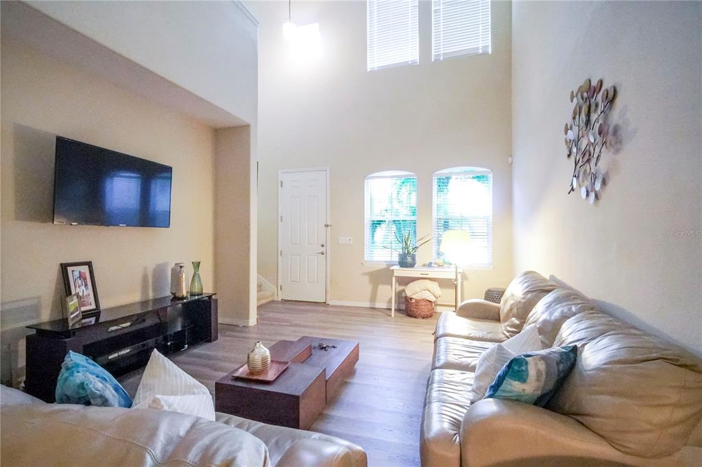 A living room features high ceilings, light wood-look flooring, and a large leather sofa — 2925 AQUA VIRGO LOOP UNIT 25, ORLANDO, FL