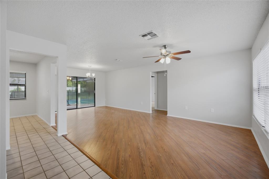 A living room with wood-look flooring, a ceiling fan, and a view of a pool — 8373 CAMPHOR DRIVE, SPRING HILL, FL