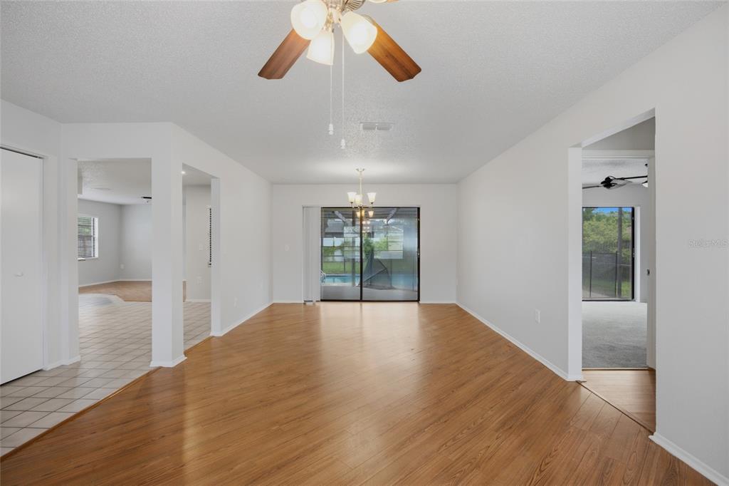 An open living area features wood-look flooring, a ceiling fan, and sliding glass doors to a pool — 8373 CAMPHOR DRIVE, SPRING HILL, FL