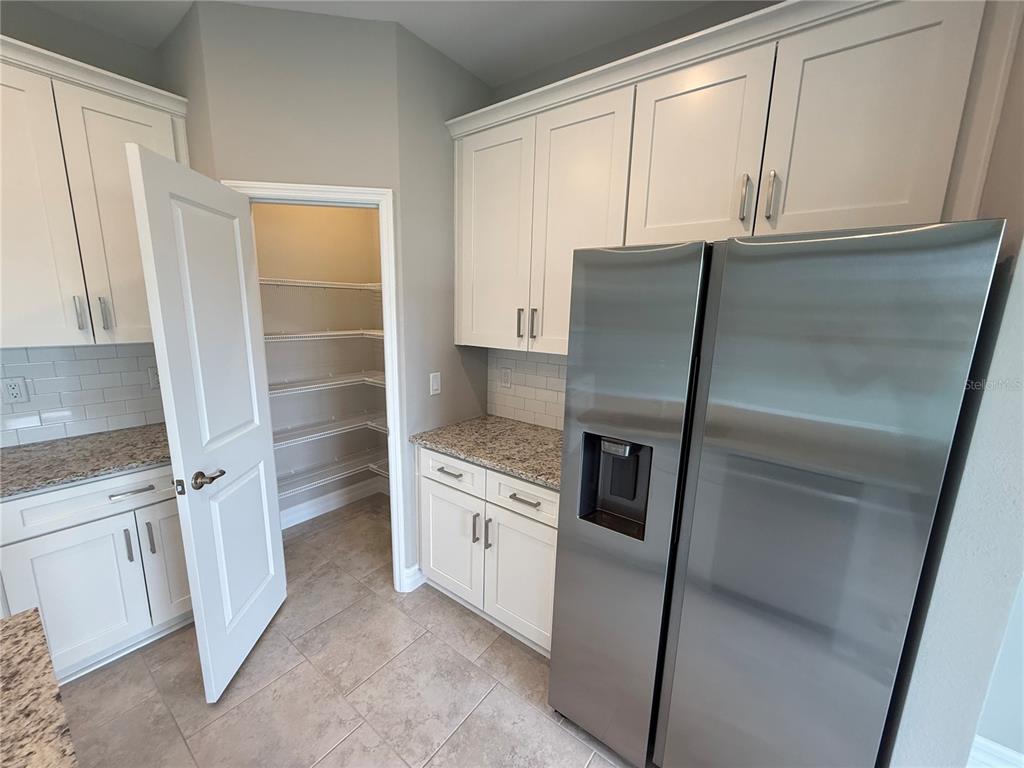 A kitchen features white cabinets, granite countertops, a stainless steel refrigerator, and a walk-in pantry — 2307 ZUYDER TERRACE, NORTH PORT, FL