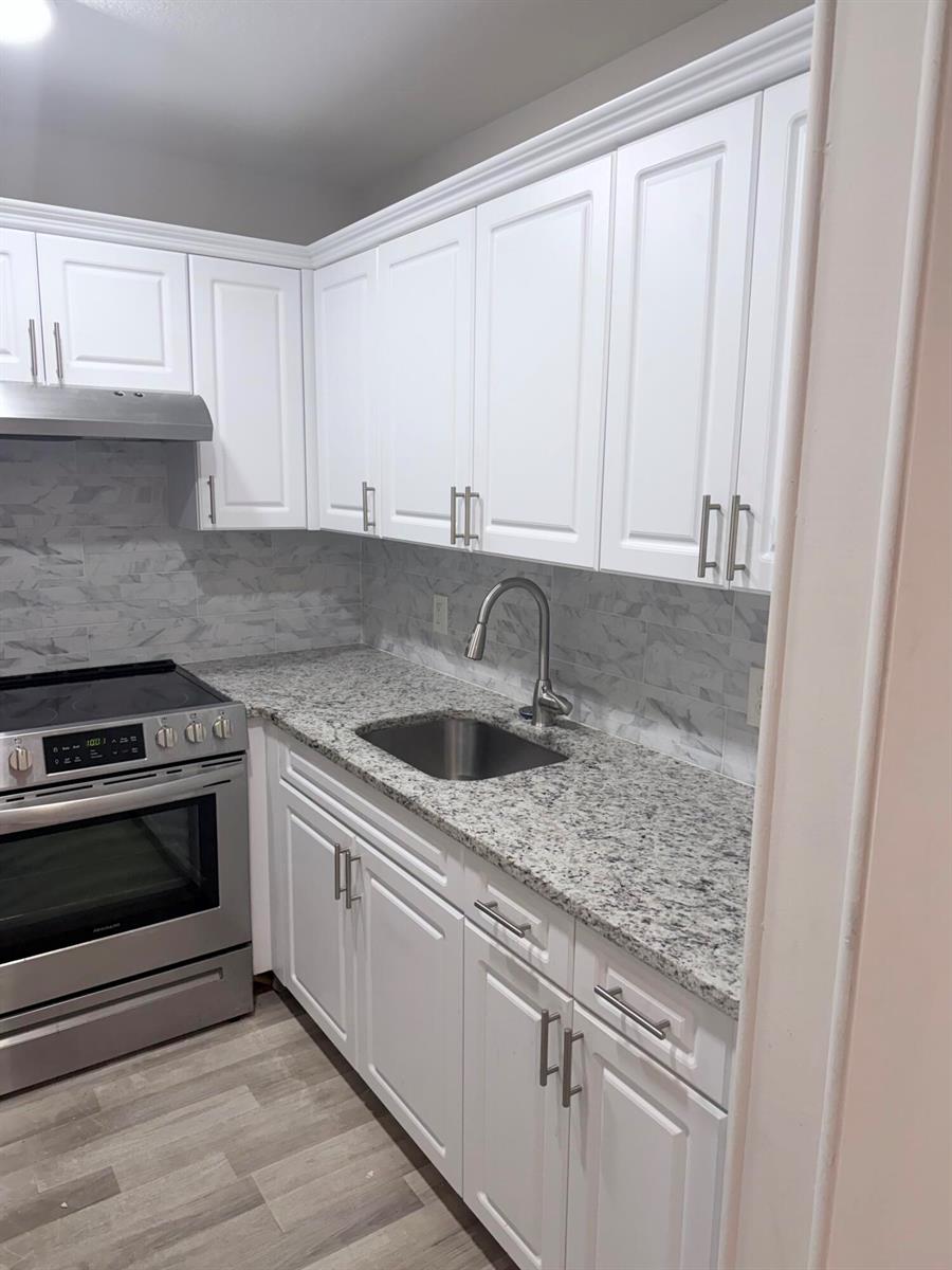 A kitchen features white cabinets, granite countertops, a stainless steel stove, and a tile backsplash — 204 Canterbury I, West Palm Beach FL 33417, WEST PALM BEACH, FL