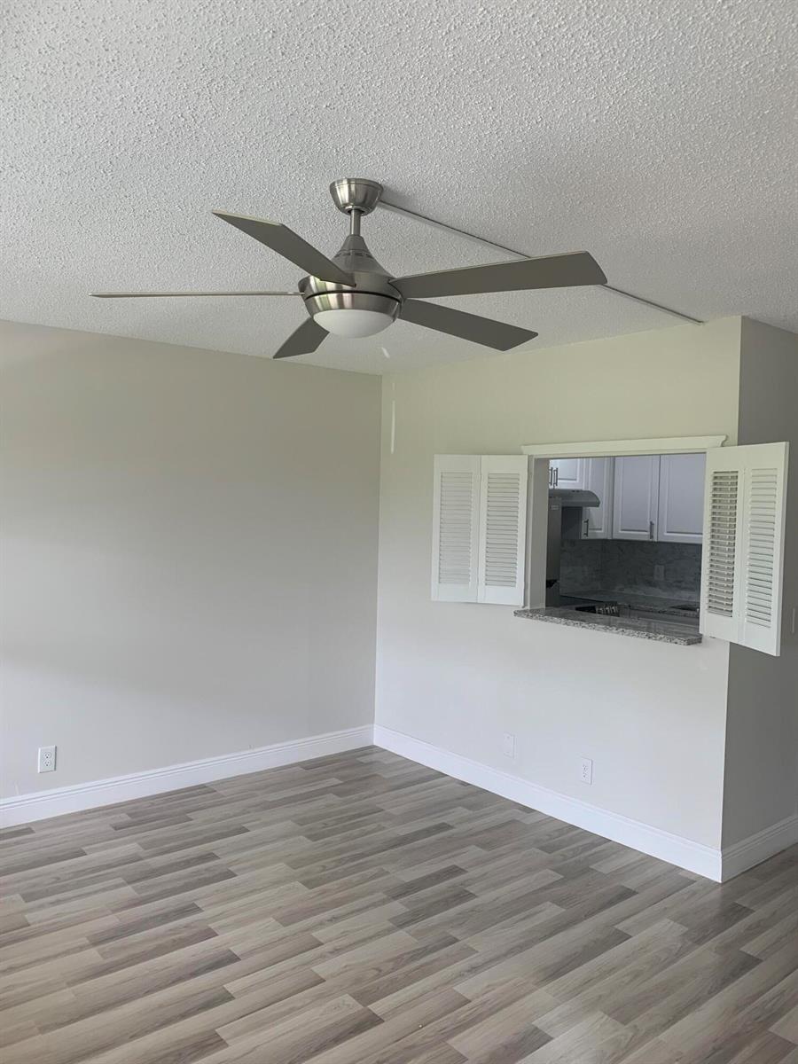 A room with light gray walls, wood-look flooring, a ceiling fan, and a kitchen pass-through window — 204 Canterbury I, West Palm Beach FL 33417, WEST PALM BEACH, FL