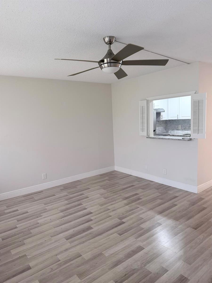 An empty room with light wood-look flooring, a ceiling fan, and a kitchen pass-through window — 204 Canterbury I, West Palm Beach FL 33417, WEST PALM BEACH, FL