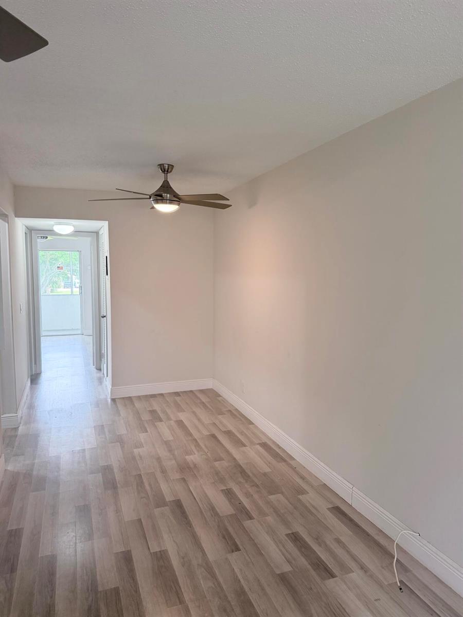 An empty room with light wood-look flooring, a ceiling fan, and a doorway to a balcony — 204 Canterbury I, West Palm Beach FL 33417, WEST PALM BEACH, FL