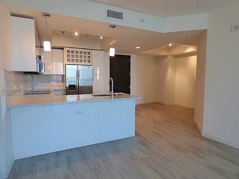 A modern kitchen features white cabinetry, stainless steel appliances, and a breakfast bar island — 999 SW 1 AVE # 1907, Miami FL 33130, MIAMI, FL