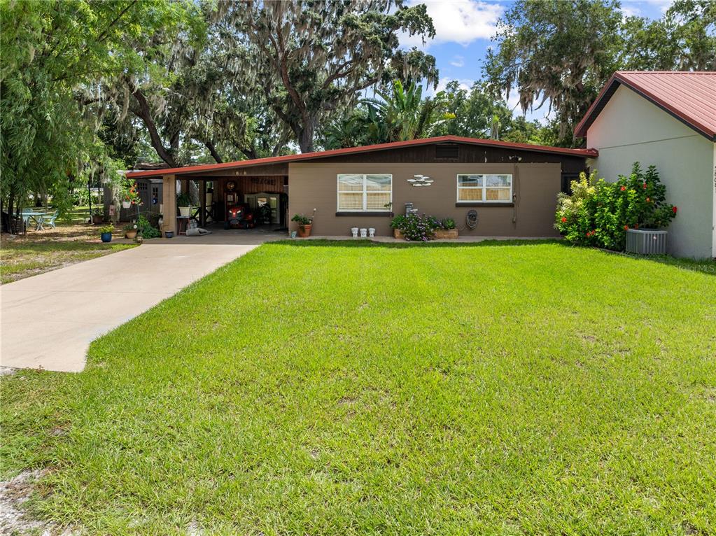 A single-story house with a brown exterior, a front carport, and a large grassy lawn — 5868 ALLIGATOR LAKE SHORE W, ST CLOUD, FL