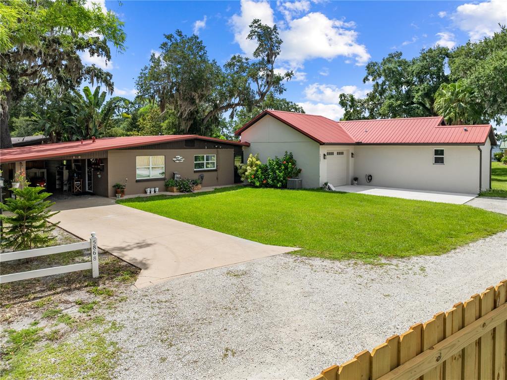 A single-story house with a red metal roof, brown siding, and a concrete driveway — 5868 ALLIGATOR LAKE SHORE W, ST CLOUD, FL