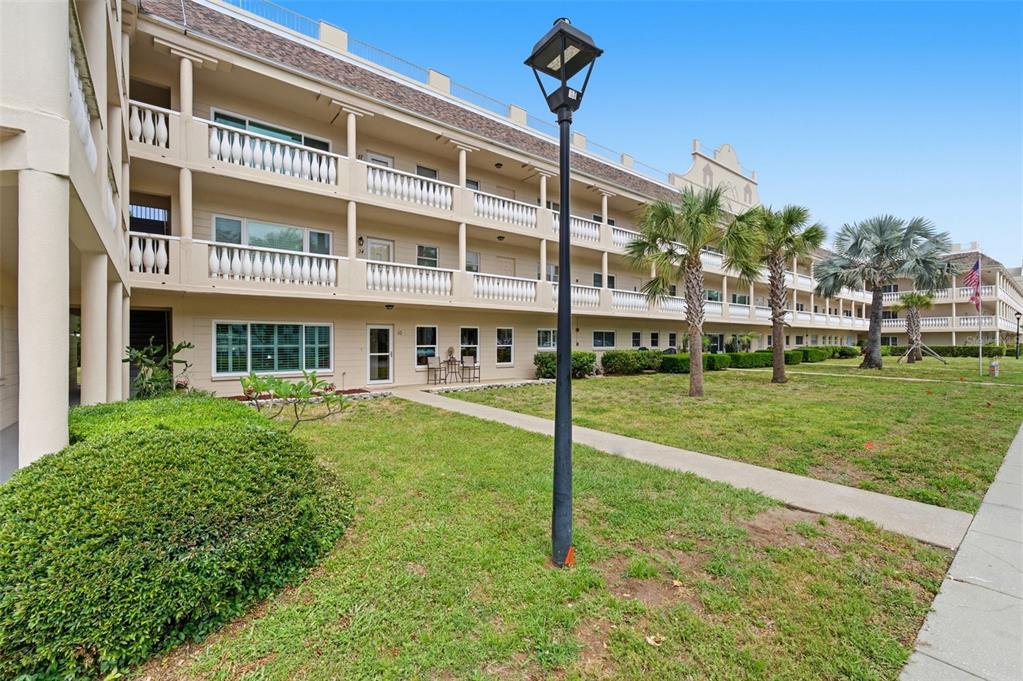 A multi-story apartment building with balconies and a grassy lawn featuring a lamp post — 2170 AMERICUS BOULEVARD S UNIT 58, CLEARWATER, FL