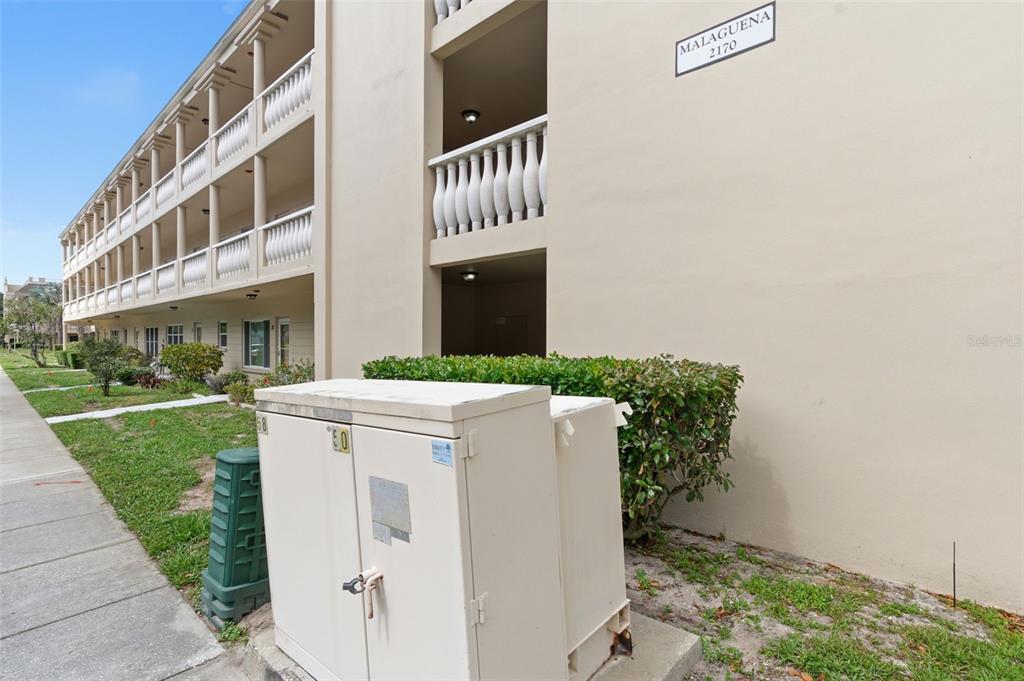 A beige multi-story apartment building exterior features a white utility box in the foreground — 2170 AMERICUS BOULEVARD S UNIT 58, CLEARWATER, FL