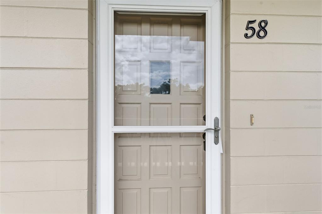 A white storm door with a glass panel is mounted on a beige exterior wall — 2170 AMERICUS BOULEVARD S UNIT 58, CLEARWATER, FL