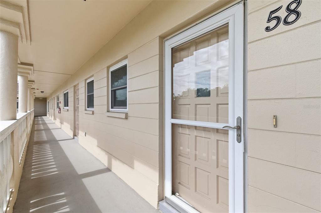 A beige exterior walkway features a white storm door with the number 58 above it — 2170 AMERICUS BOULEVARD S UNIT 58, CLEARWATER, FL
