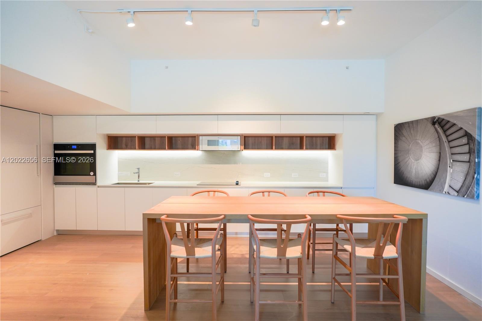 A modern kitchen features white cabinetry, a long wooden dining table, and track lighting — 10250 Collins Avenue # 412, Bal Harbour FL 33154, BAL HARBOUR, FL