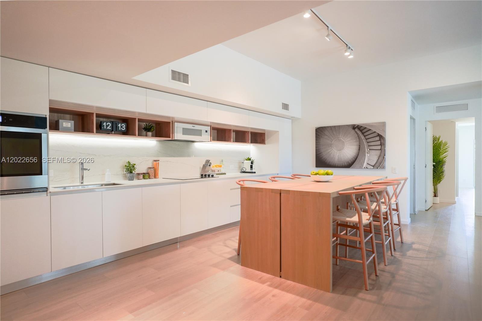 A modern kitchen features white cabinetry, light wood accents, and a central wooden dining island — 10250 Collins Avenue # 412, Bal Harbour FL 33154, BAL HARBOUR, FL