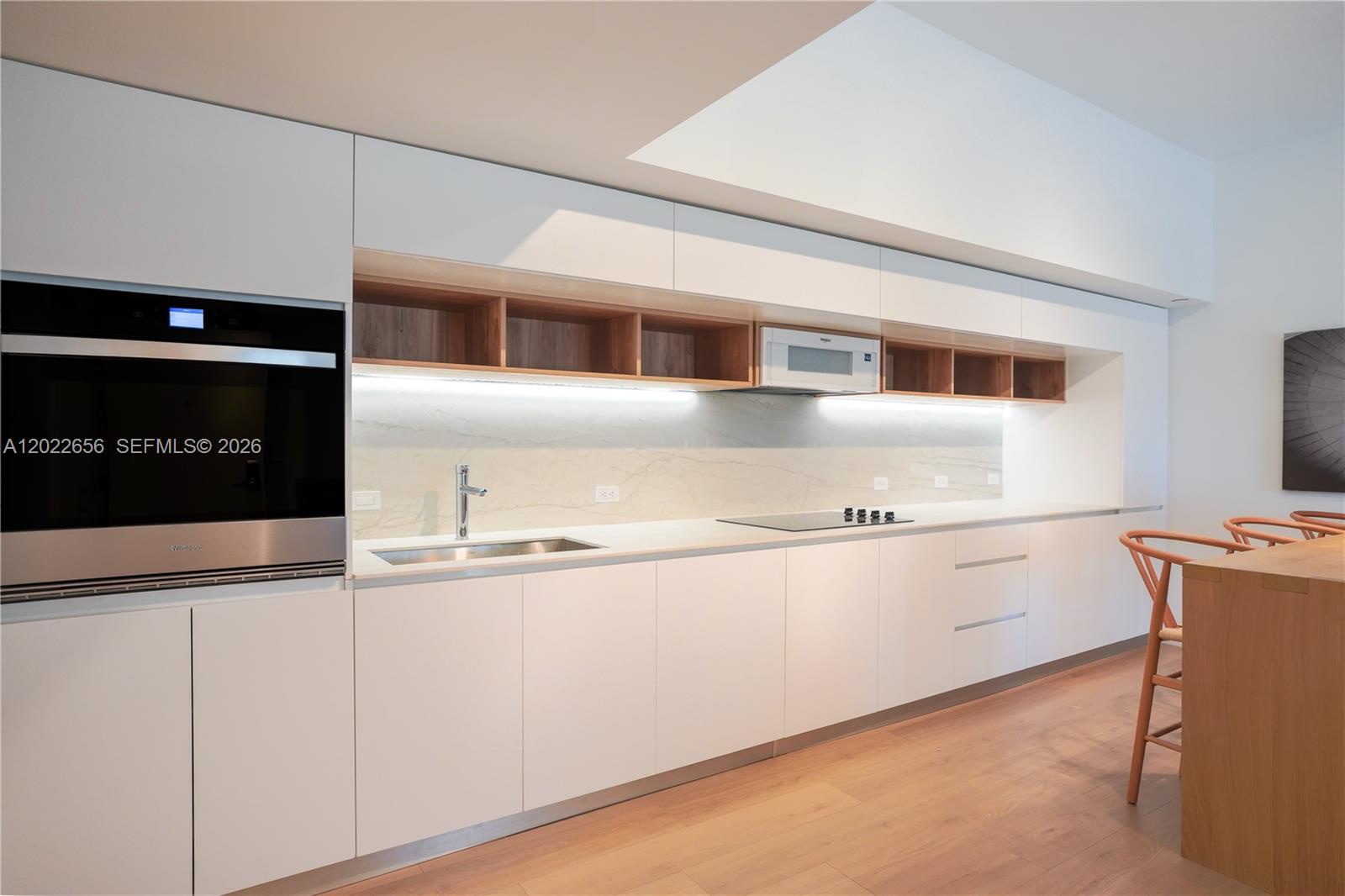 A modern kitchen features white flat-panel cabinetry, open wood shelving, and a marble backsplash — 10250 Collins Avenue # 412, Bal Harbour FL 33154, BAL HARBOUR, FL