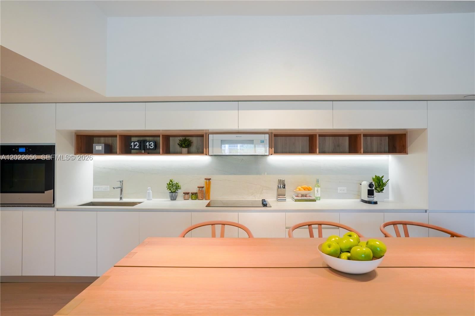 A modern kitchen features white cabinetry, wood-toned open shelving, and a light-colored stone backsplash — 10250 Collins Avenue # 412, Bal Harbour FL 33154, BAL HARBOUR, FL