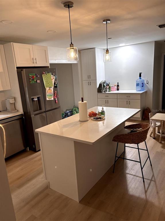 A modern kitchen features white cabinetry, a central island with a stool, and stainless appliances — 6016 18TH STREET NE, ST PETERSBURG, FL