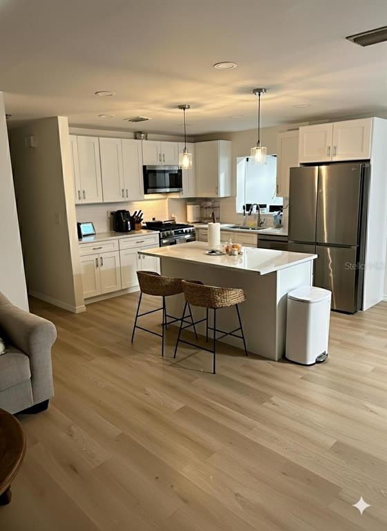 A modern kitchen features white cabinetry, a central island with bar stools, and stainless appliances — 6016 18TH STREET NE, ST PETERSBURG, FL