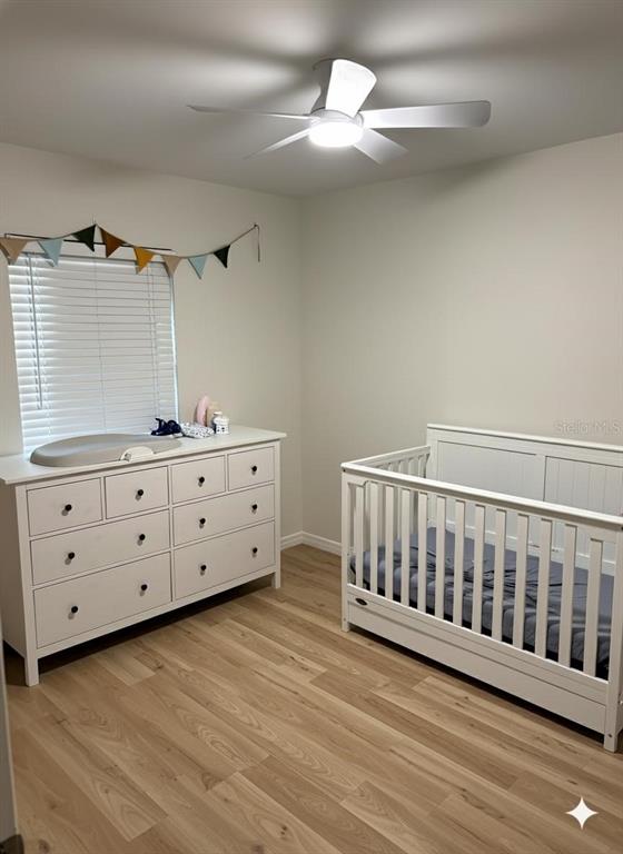 A nursery features a white crib, a matching dresser with a changing pad, and wood flooring — 6016 18TH STREET NE, ST PETERSBURG, FL
