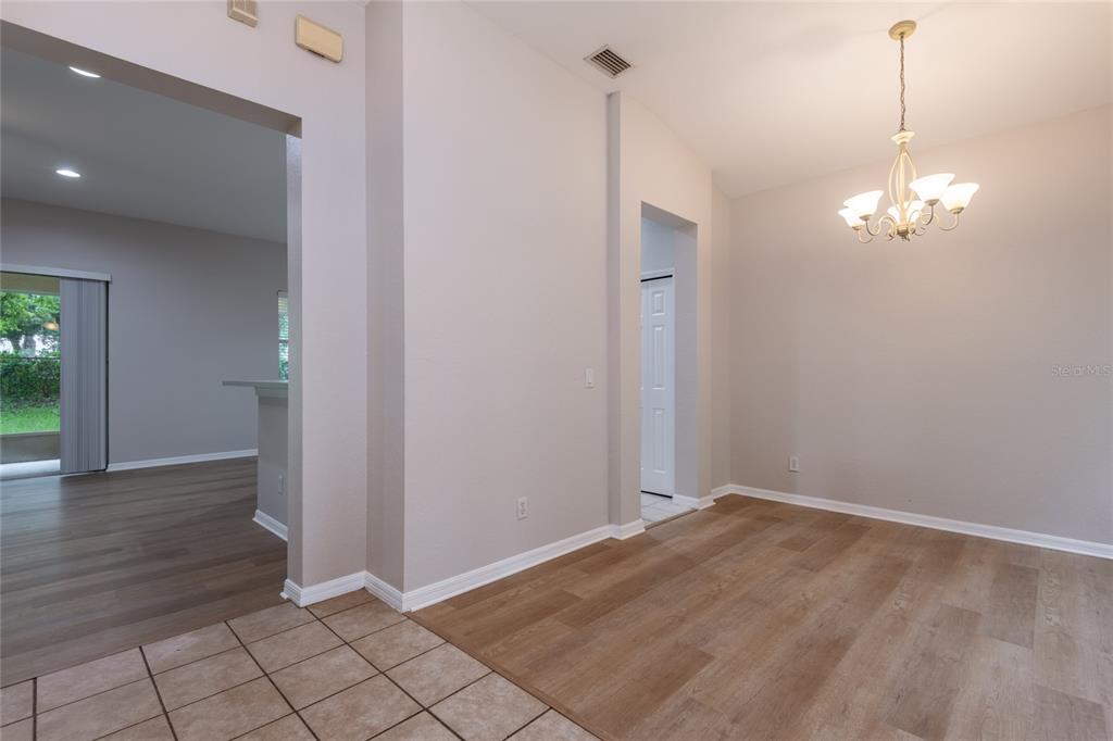 A dining area with wood-look flooring and a chandelier adjacent to a tiled kitchen space — 11112 HOLLY CONE DRIVE, RIVERVIEW, FL