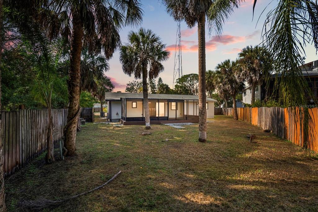 A backyard view of a single-story house with a screened porch and palm trees — 10395 SAN MARTIN BOULEVARD NE, ST PETERSBURG, FL