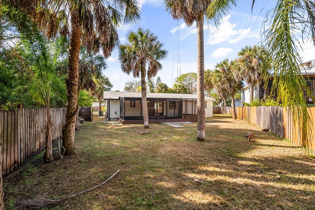 A backyard with a screened-in porch, palm trees, and wooden privacy fences on both sides — 10395 SAN MARTIN BOULEVARD NE, ST PETERSBURG, FL