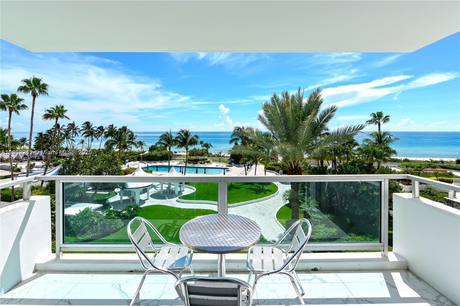 A balcony with a small table and chairs overlooks a pool, palm trees, and ocean — 5151 Collins Ave # 619, Miami Beach FL 33140, MIAMI BEACH, FL