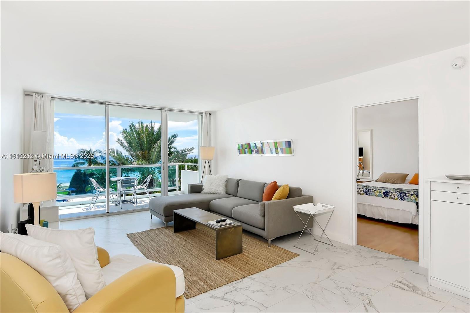 A living room with a gray sectional sofa, marble floors, and a balcony overlooking the ocean — 5151 Collins Ave # 619, Miami Beach FL 33140, MIAMI BEACH, FL